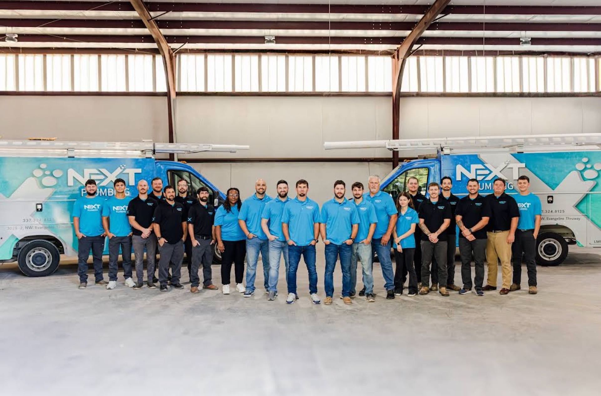 The Next Plumbing team standing in front of two of their service vans